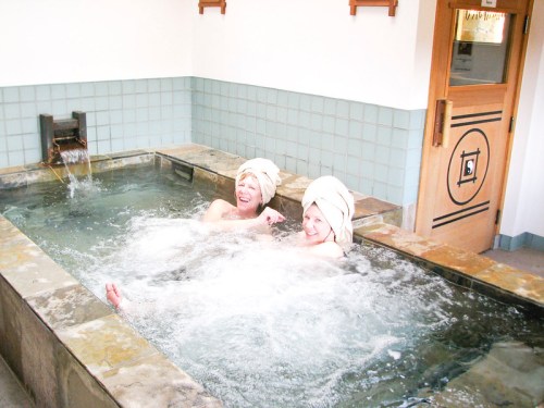 Two people in towels relax in a bubbling hot tub, enjoying a spa-like atmosphere.