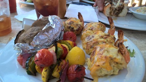 A plate of shrimp stuffed with cheese, grilled vegetables, a baked potato, and a lemon wedge.