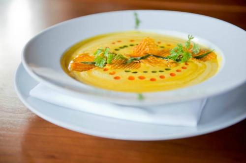 A bowl of creamy soup garnished with herbs and colorful dots, served on a white plate with a napkin underneath.