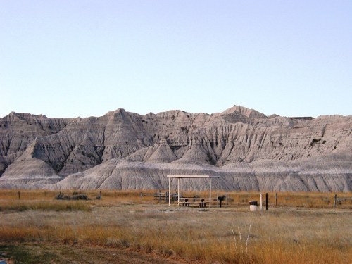 A vast landscape featuring gray, rugged hills and a small picnic area with a shelter in the foreground.