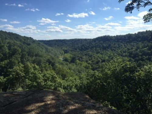 A scenic view of a lush green valley surrounded by hills under a blue sky with scattered clouds.