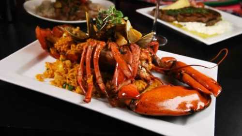 A vibrant plate of lobster with rice, clams, and garnishes, served on a white dish against a dark background.