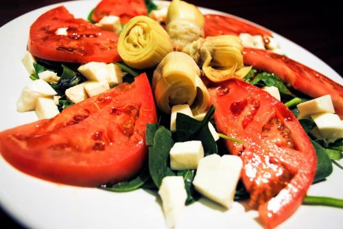 A colorful salad featuring sliced tomatoes, artichoke hearts, and cubes of cheese on a bed of greens.