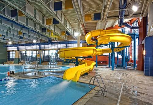 Indoor swimming pool featuring two yellow water slides and a whirlpool area, with colorful ceiling panels.
