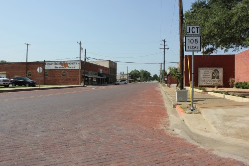 A quiet street in Texas with brick pavement, storefronts, and a road sign for Junction 108.