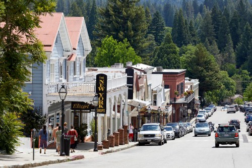 A charming street lined with shops and trees, featuring people walking and cars parked along the road.