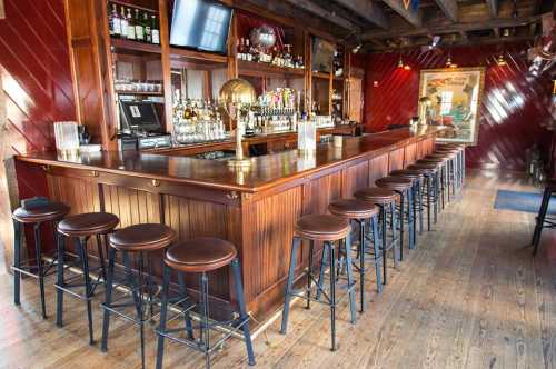 A wooden bar with high stools, shelves of liquor, and a warm, inviting atmosphere in a rustic setting.