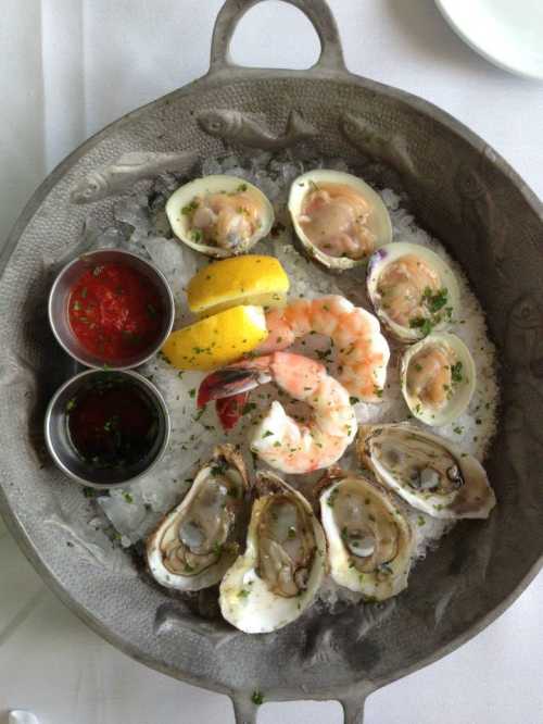 A seafood platter featuring oysters, shrimp, and lemon, served on ice with dipping sauces.