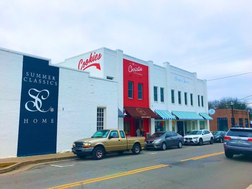 A street view of a charming storefront with "Cookies" and "Summer Classics" signs, featuring parked cars in front.
