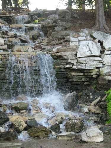 A serene waterfall cascading over rocky terrain, surrounded by lush greenery and trees.