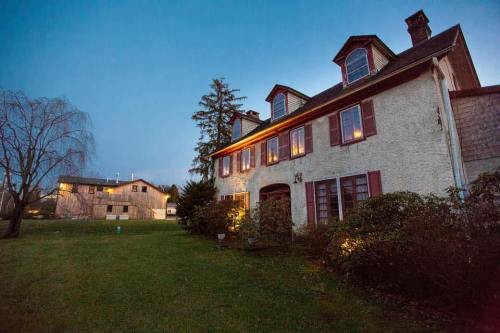 A charming two-story house with red shutters, illuminated at dusk, surrounded by a grassy yard and trees.