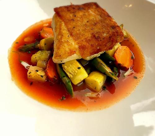 A beautifully plated dish featuring a piece of fish atop colorful sautéed vegetables in a rich sauce.