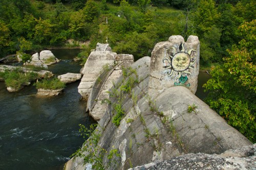 A concrete structure with a sun mural, surrounded by greenery and a flowing river.