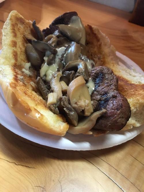 A toasted sandwich filled with sliced beef, mushrooms, and a creamy sauce on a paper plate.