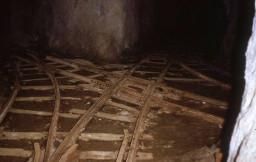 Dimly lit underground mine with wooden railway tracks intersecting on the ground.
