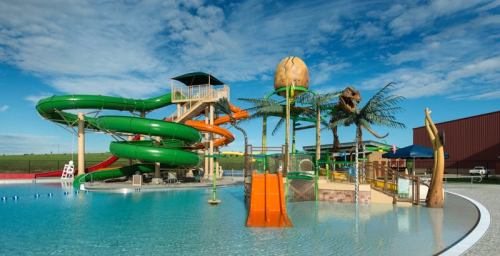 Colorful water slides and play structures by a pool under a blue sky with scattered clouds.