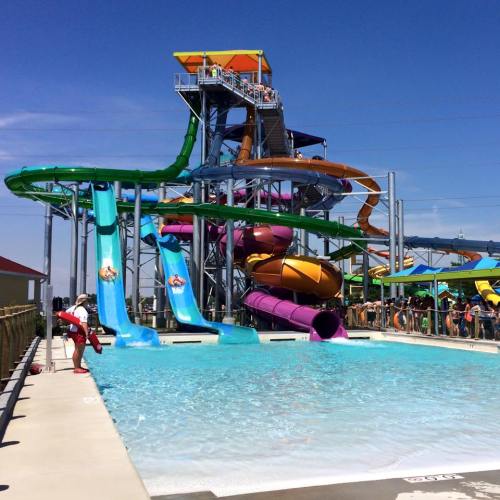 A vibrant water park featuring colorful slides and a large pool, with people enjoying the sunny day.