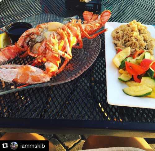 A plate featuring a lobster with dipping sauce and a side of rice and sautéed vegetables on a table.