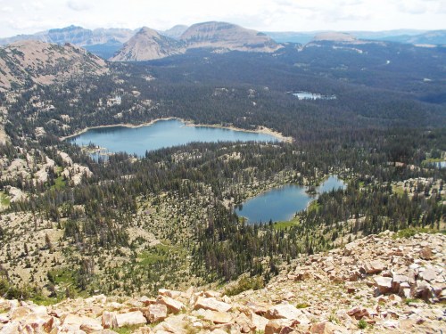 A panoramic view of a mountainous landscape with several lakes surrounded by dense forests and rocky terrain.