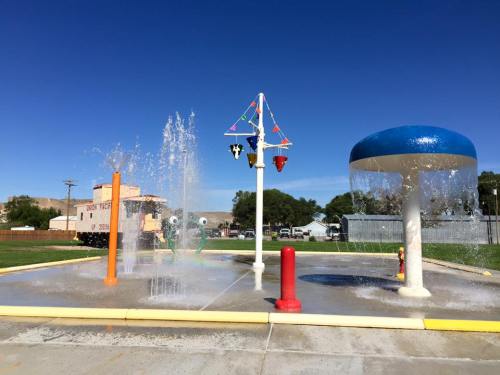 A colorful splash pad with water features, including fountains and a large mushroom-shaped sprinkler, under a clear blue sky.
