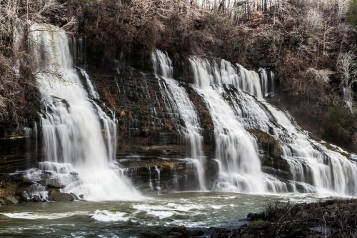 A cascading waterfall flows over rocky cliffs, surrounded by trees and a serene landscape.