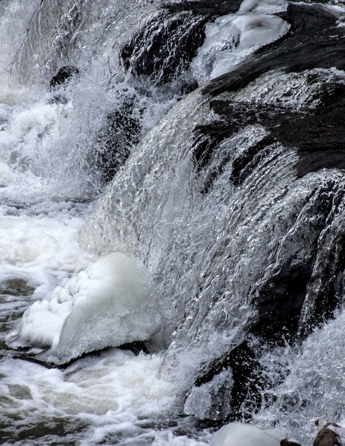 Close-up of cascading water over rocks, creating foam and splashes in a natural setting.