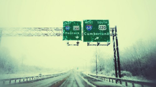 Snowy highway sign indicating directions to Hancock and Cumberland on Interstate 68.