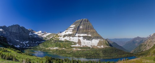 A panoramic view of a majestic mountain with snow-capped peaks, surrounded by lush greenery and a serene lake.