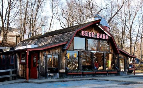 A rustic restaurant named "Beef Barn" with large windows, surrounded by trees and a clear blue sky.