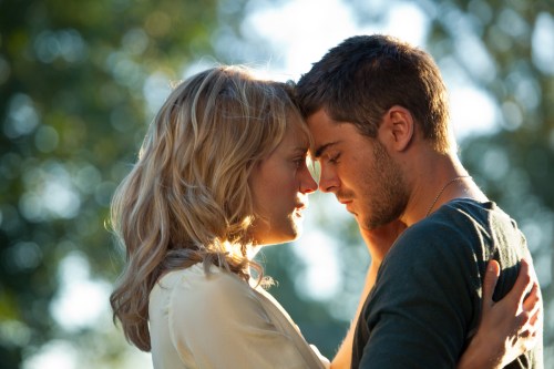 A couple shares a tender moment, foreheads touching, in a sunlit outdoor setting.