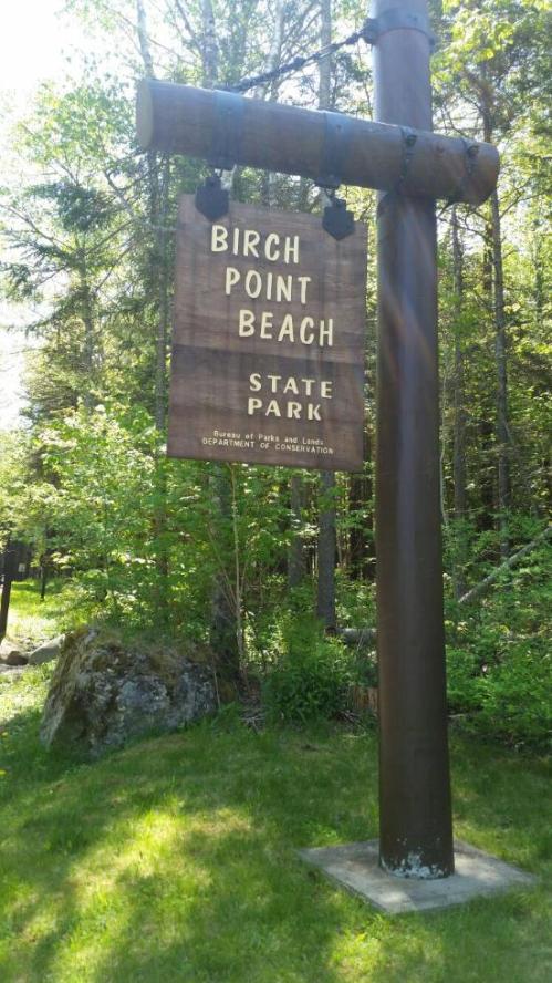 Sign for Birch Point Beach State Park surrounded by greenery and trees.