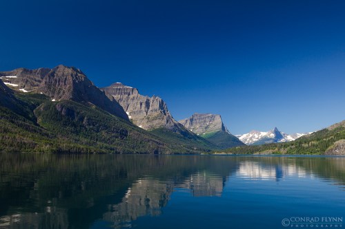 A serene lake reflects majestic mountains under a clear blue sky, showcasing nature's beauty and tranquility.