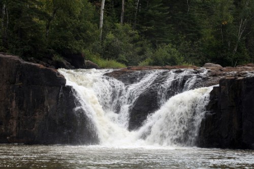 A serene waterfall cascading over rocky cliffs, surrounded by lush green trees and a calm river below.