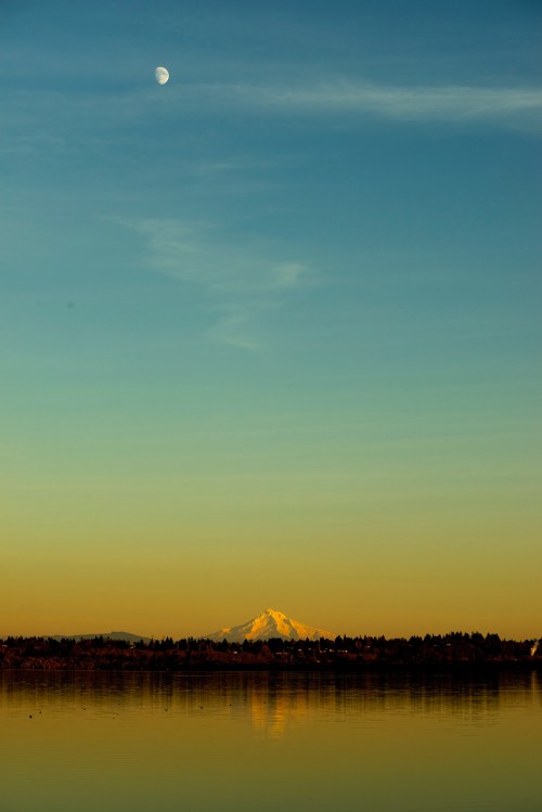 A serene landscape featuring a snow-capped mountain, a clear sky, and a crescent moon reflected in calm water.