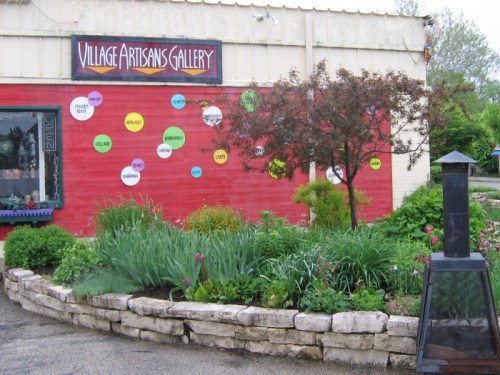 A colorful gallery exterior with a sign, vibrant wall decorations, and a landscaped garden in front.