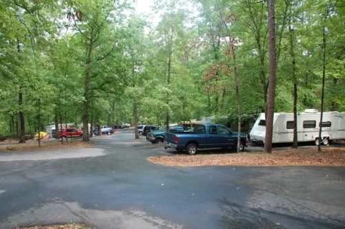 A wooded campground with several parked cars and RVs along winding roads surrounded by green trees.