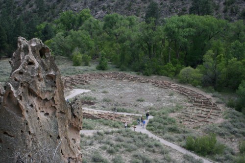 Aerial view of a circular stone structure surrounded by greenery, with people walking along a path nearby.