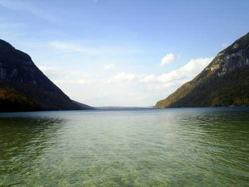 A serene lake surrounded by mountains under a clear blue sky, with calm waters reflecting the landscape.