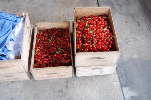 Three wooden crates filled with fresh red cherries, sitting on a concrete floor.