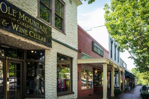 A charming street view featuring shops, including Ole Mountain Collectors & Wine Cellar, under a clear blue sky.
