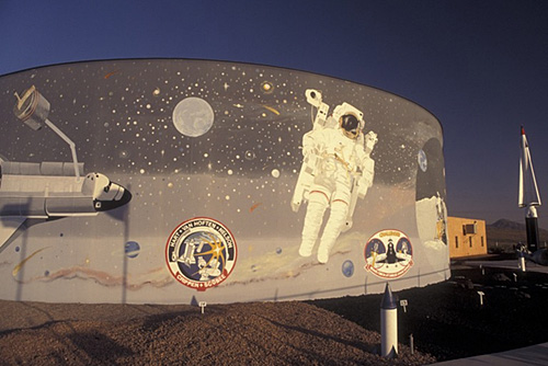 Mural depicting an astronaut in space, with planets and spacecraft, on a building in a desert landscape.