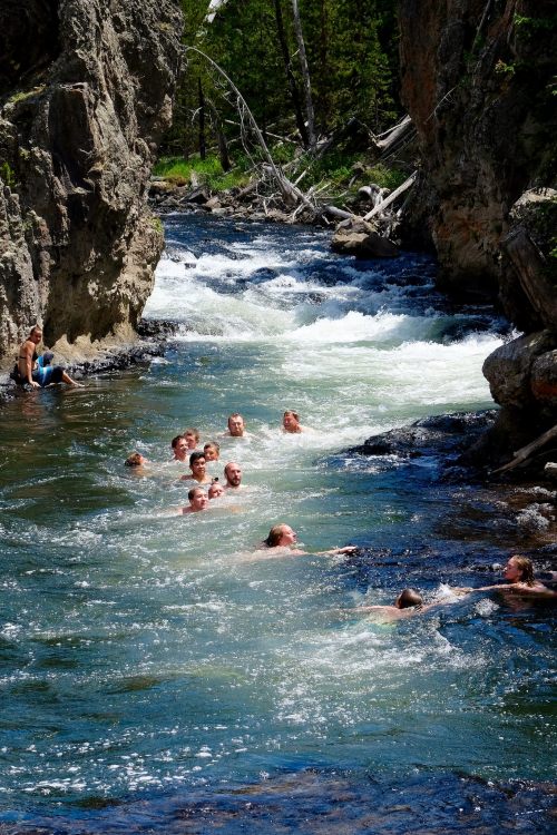 A group of people swimming in a clear, flowing river surrounded by rocky cliffs and lush greenery.