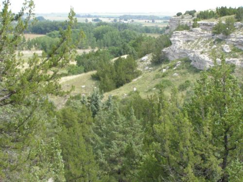 A scenic view of rolling hills and greenery, featuring rocky cliffs and a lush landscape under a cloudy sky.