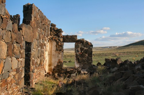 Ruins of a stone structure with a grassy landscape and blue sky in the background.