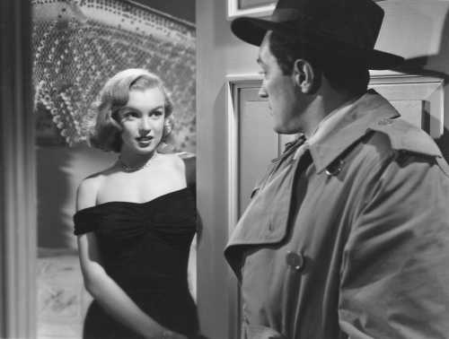 A glamorous woman in a black dress stands in a doorway, gazing at a man in a trench coat. Classic film noir scene.