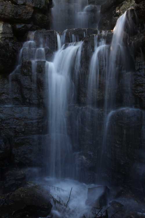 A serene waterfall cascading over rocky cliffs, surrounded by dark stones and gentle mist.