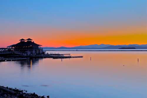 A serene sunset over calm waters, with a silhouette of a building and mountains in the background.