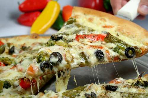 A slice of cheesy vegetable pizza with peppers, olives, and broccoli being lifted from a tray.