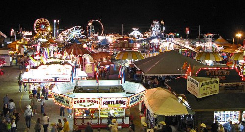A vibrant night scene of a fair with colorful lights, food stalls, and rides bustling with people.