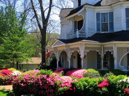 A charming Victorian house with intricate architecture, surrounded by vibrant blooming flowers and greenery.